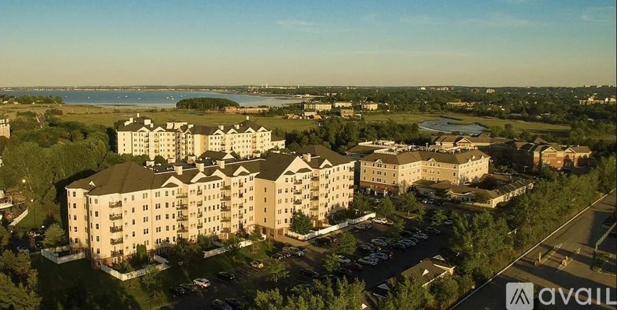 A large apartment complex is situated in a green area with a body of water in the distance.