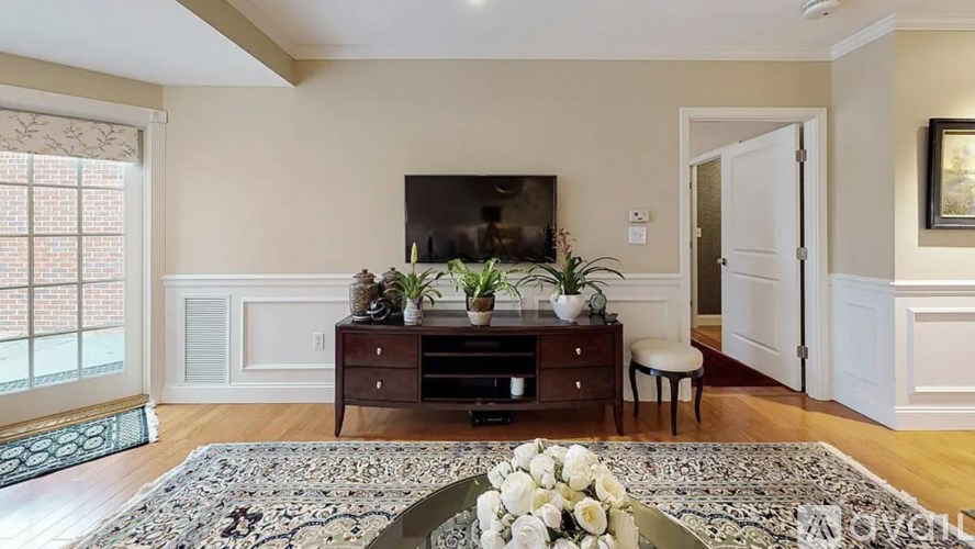 A living room with a television, a rug, and a vase of flowers.