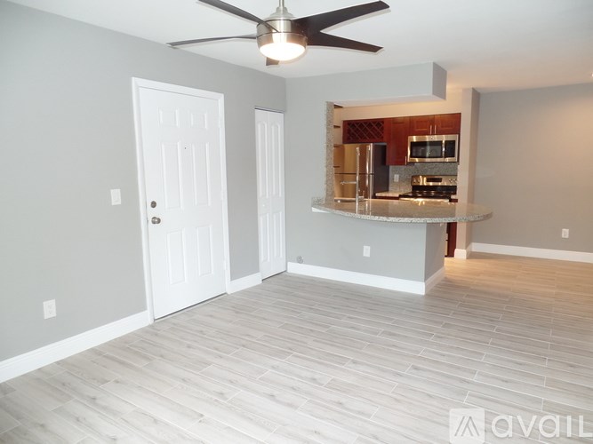 A room with a ceiling fan and a kitchen area in the background.