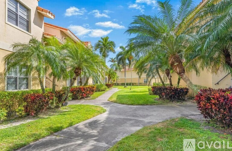 A residential area with a pathway, palm trees, and red shrubbery.