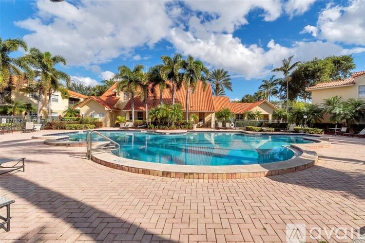 A large outdoor swimming pool surrounded by a brick patio and palm trees.