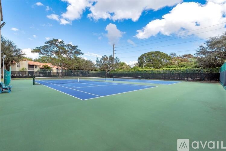 A tennis court with a blue and green surface is surrounded by a fence and trees.
