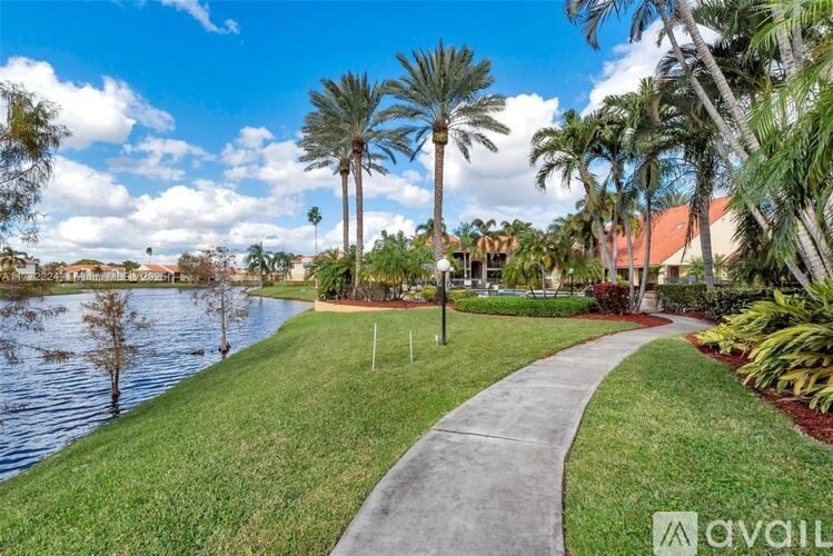A pathway leads through a grassy area with palm trees and a body of water.