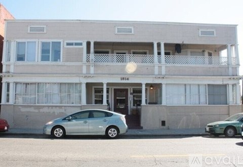 A silver car is parked in front of a two-story building with a balcony.