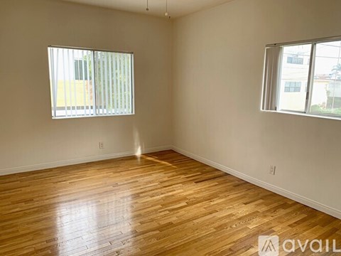A room with wooden flooring and two windows.