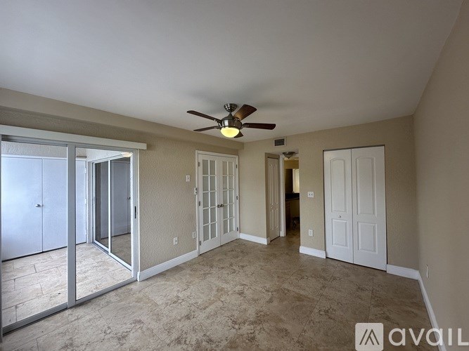 A spacious room with a ceiling fan and sliding glass doors leading to a balcony.