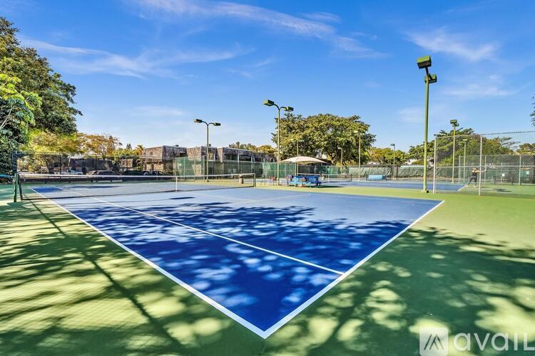 A tennis court with a blue surface and white lines, surrounded by a fence and trees.