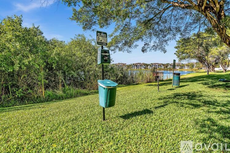 A signpost stands in a grassy area with trees and a blue bin in the background.