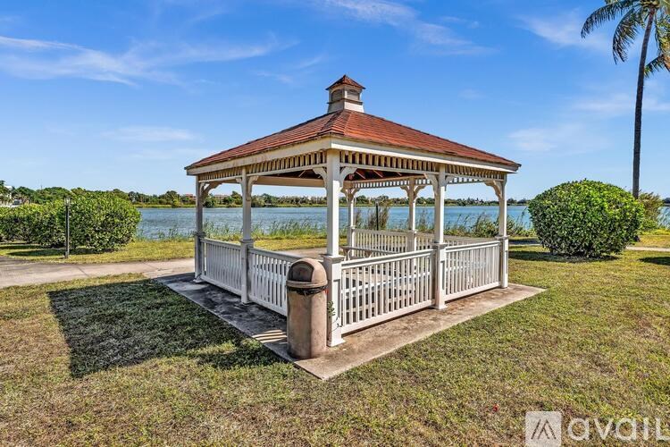 A gazebo with a red roof is situated in a grassy area with a body of water in the background.