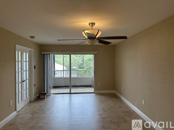 A spacious room with a ceiling fan and sliding glass doors leading to a balcony.