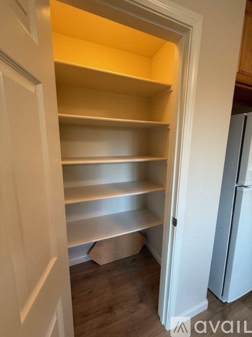 Empty shelves in a kitchen with a refrigerator in the background.