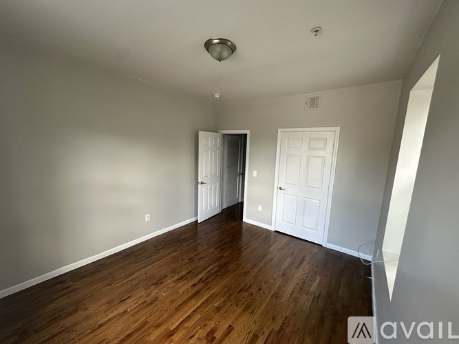 A room with wooden floors and white walls, with a door on the left and a window on the right.