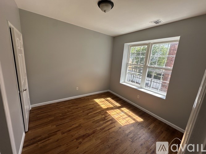 A room with wooden flooring and a window letting in sunlight.