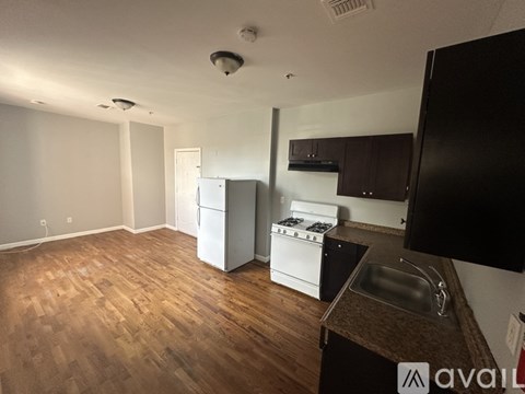 A kitchen with a white fridge and stove, wooden floors, and a black cabinet.