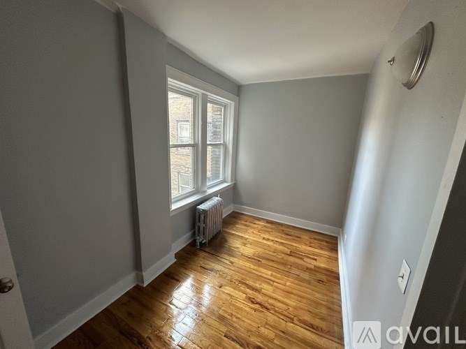 A room with wooden flooring and a window with a radiator beneath it.