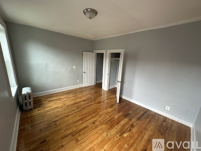 A room with wooden floors and white walls, with a doorway leading to another room.