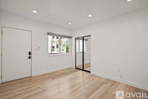 A spacious room with a white door, a window with a view of a building, and a wooden floor.