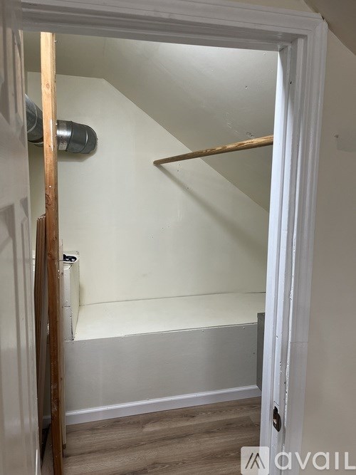 A white doorway opens to a small, empty room with a wooden plank on the wall.