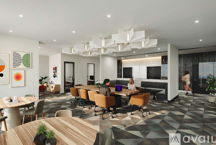 A modern office space with a large table and chairs in the center, and people working at their desks.