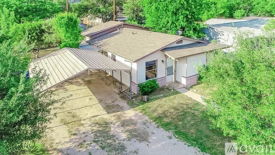 A house with a brown roof and a white exterior is surrounded by greenery.