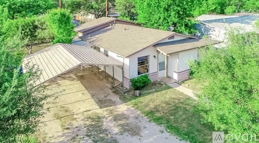 A house with a brown roof and a white exterior is surrounded by greenery.