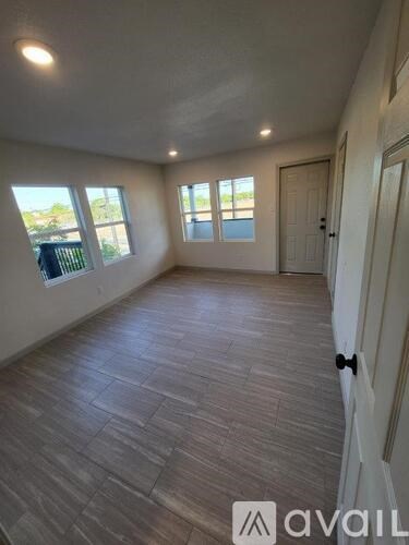 A room with wooden flooring and two windows.