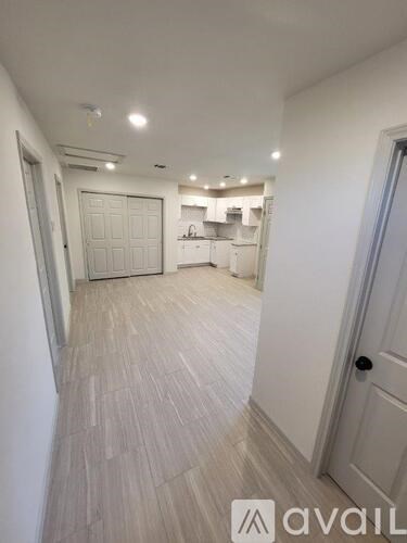 A hallway with a white door and a white cabinet with a white fridge and microwave.