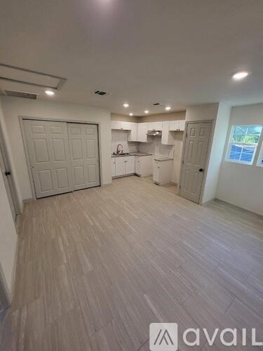 A spacious room with light wood flooring and white walls.