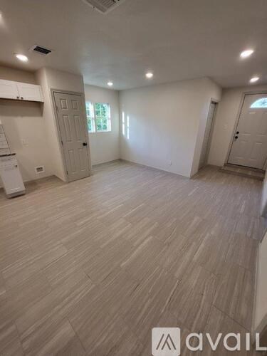 A room with wooden flooring and white walls, with a window on the right wall.