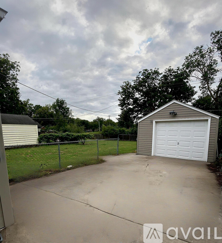 A detached garage with a white door is surrounded by a fence and a grassy area.