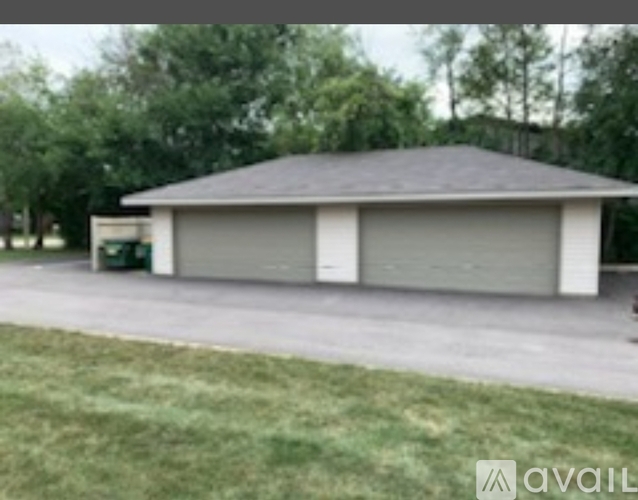 A two-car garage with a grey roof and a green trash can in front of it.