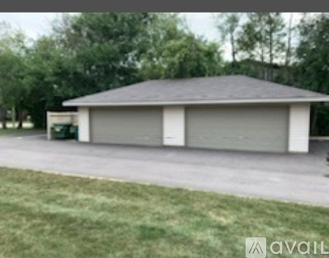 A two-car garage with a grey roof and a green trash can in front of it.