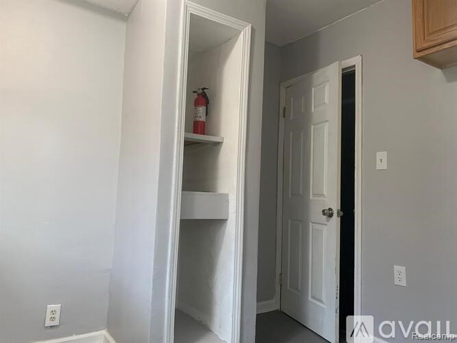 A white door is open to a hallway with a fire extinguisher on a shelf.