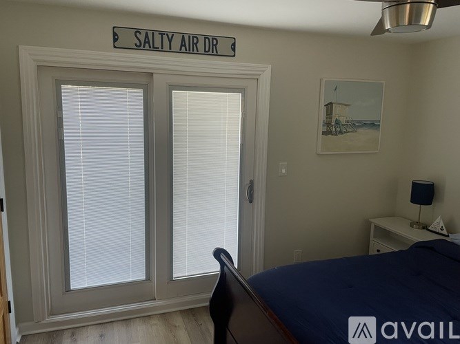 A bedroom with a bed, a window with blinds, a nightstand, and a painting on the wall.