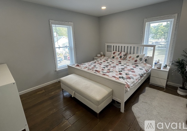A bedroom with a white bed and a window with blinds.