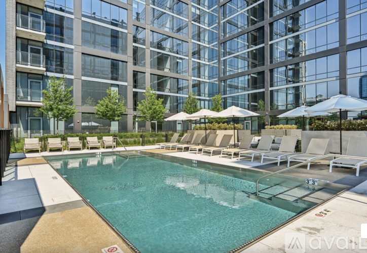 A large swimming pool surrounded by lounge chairs and umbrellas in front of a modern building.