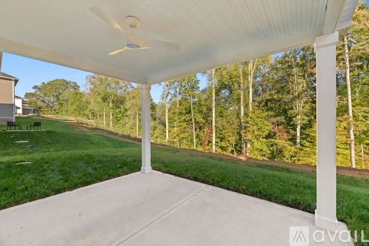 A covered patio area with a ceiling fan and a view of a grassy area and trees.