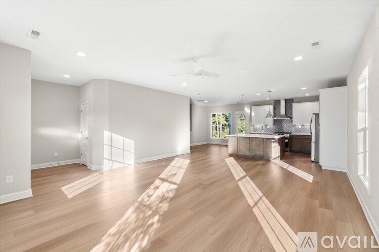 A spacious living room with wooden flooring and a kitchen area in the background.
