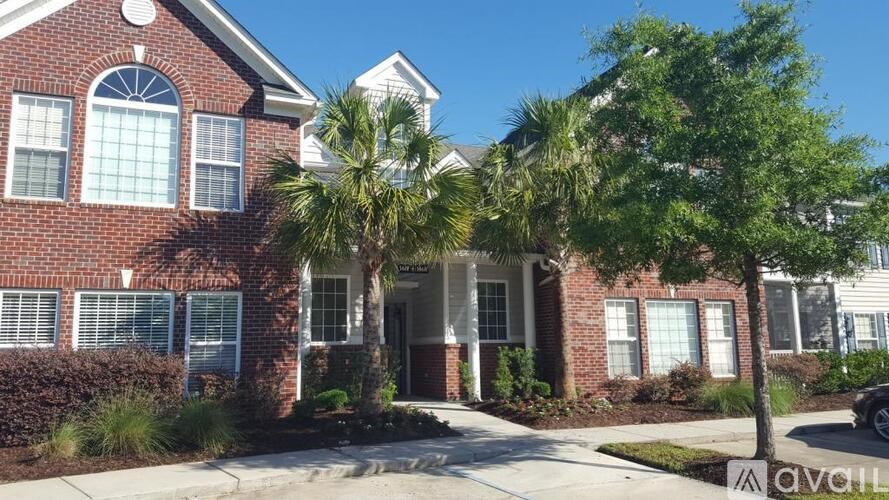 A house with a red brick facade and a white roof with a palm tree in front.