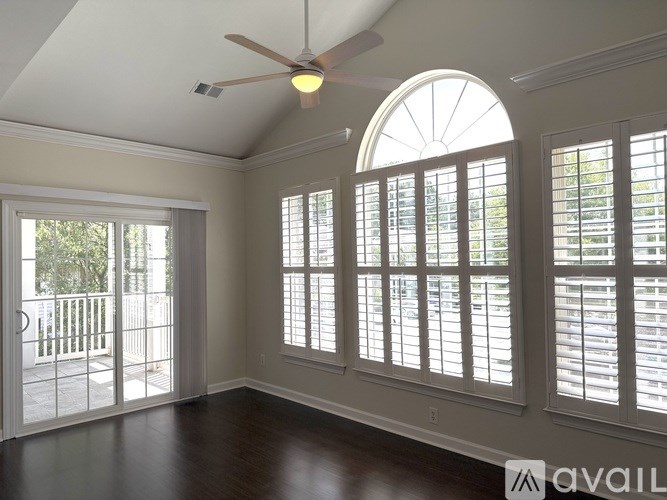 A room with a ceiling fan and large windows.