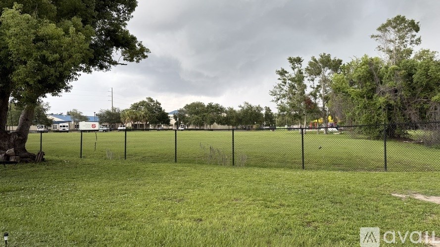 A grassy field with a fence and trees in the distance under a cloudy sky.