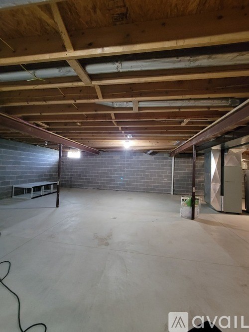 A spacious unfinished room with a concrete floor and exposed wooden beams on the ceiling.