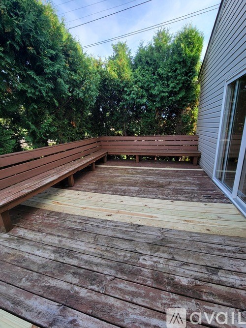 A wooden deck with a bench and trees in the background.