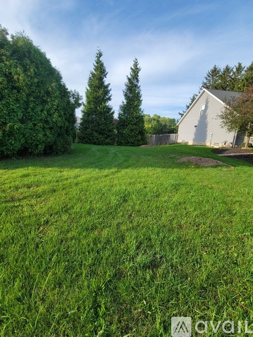 A grassy field with a house and trees in the background.