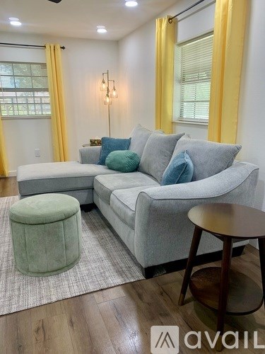 A living room with a grey couch, a green ottoman, and a wooden table.