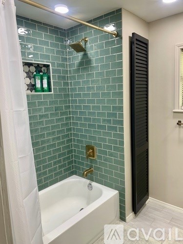 A white bathtub with a gold faucet is in a bathroom with green tiles.