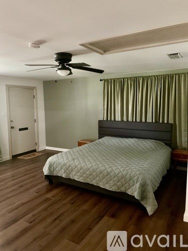 A bedroom with a bed, ceiling fan, and wooden floors.
