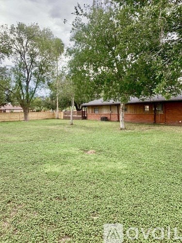 A grassy field with trees and a building in the background.