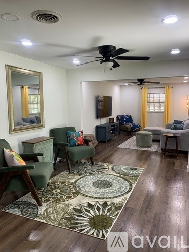 A living room with a rug, chairs, and a ceiling fan.