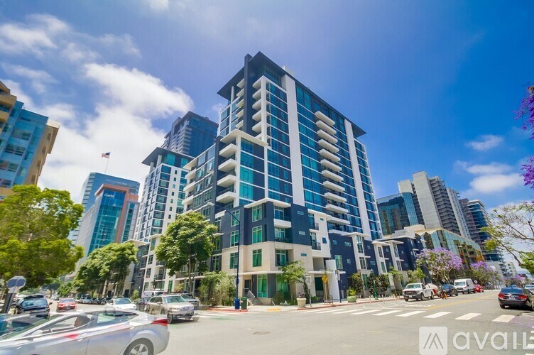 A modern multi-story building with a blue and white exterior is surrounded by trees and other buildings.